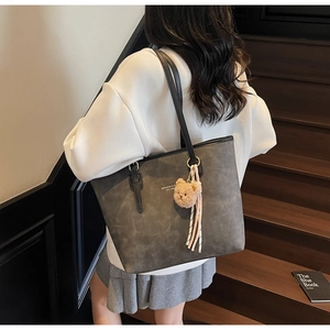 Grey large tote bag with bear charm and pink tassel worn over the shoulder by a model