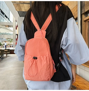 Detail of coral nylon backpack with convertible zipper strap shown on a model outdoors
