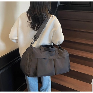 Rear view of a model carrying a large dark grey travel bag on indoor steps