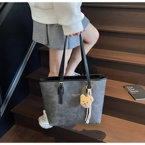Detail of grey matte tote bag with teddy bear charm and elegant tassels on wooden stairs