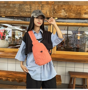 Detail of bright coral nylon chest bag with drawstring front pocket and adjustable strap
