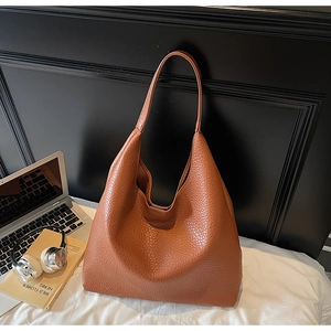 Brown leather tote bag next to a laptop and headphones in a professional office setting