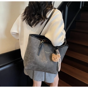 Detail of dark grey tote bag featuring matte leather texture and plush bear charm