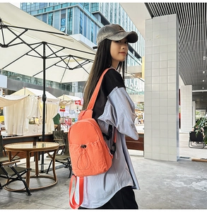 Outdoor urban shot of a small orange nylon backpack with drawstring pocket and black straps