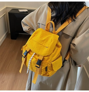 Detail view of a bright yellow nylon backpack with buckle closures and white drawstrings