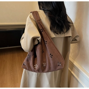 Detail of hollow floral pattern on a brown suede Hobo shoulder bag worn with a trench coat