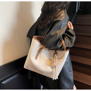 Detail of a large cream tote bag with brown handles and a cute plush bear pendant on a model