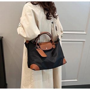 Detail view of black nylon tote bag with brown leather handles worn by model in casual style