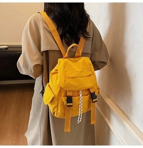 Mochila de nailon amarilla para mujer combinada con una gabardina beige elegante