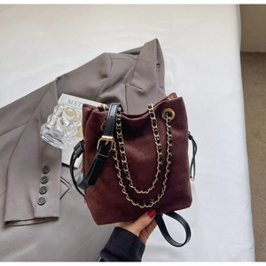 Détail du sac seau en daim marron foncé avec chaîne dorée et bandoulière en cuir noir