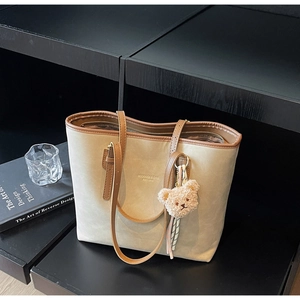 Close-up of beige tote bag with brown straps, bear charm and black-white ribbon detail