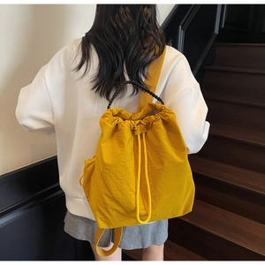 Vista posteriore di uno zaino giallo casual con coulisse su modella e manico intrecciato