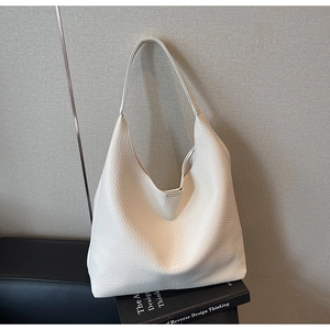 Close-up of white lychee grain leather hobo tote bag placed on books in a modern setting