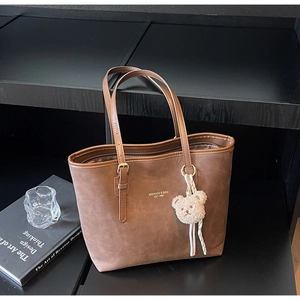 Detailed shot of brown matte tote bag with gold logo and plush bear charm accessory