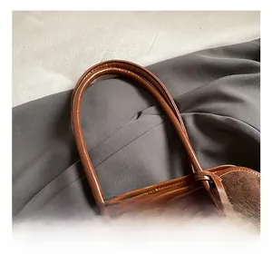 Detail of dark brown faux suede tote with cylindrical handle and plush bear charm