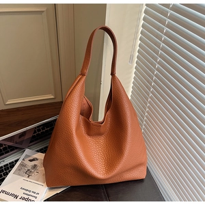 Close-up of caramel leather tote bag with lychee texture on a minimalist office desk