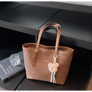 Detailed macro of brown suede tote bag with golden logo and cute plush bear charm