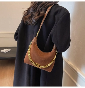 Detailed back view of dark brown suede hobo bag with chunky gold chain on a black coat