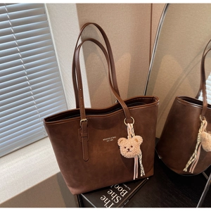 Detail of dark brown matte tote bag with teddy bear charm and sleek shoulder strap