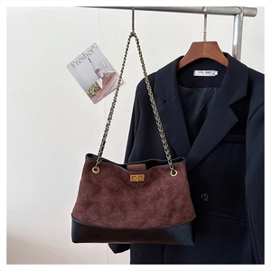 Detail of burgundy suede tote with quilted stitching and gold chain strap on blazer