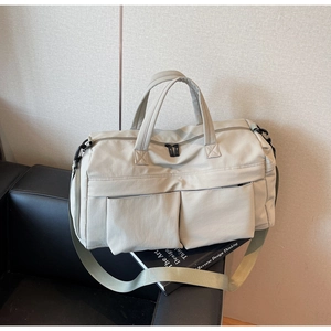 Close-up of cream travel bag with dual front pockets on leather sofa