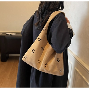 Detail of laser-cut floral patterns on khaki suede shoulder bag worn with black coat
