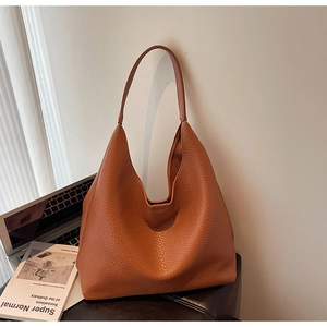 Macro detail of the orange pebbled leather texture and flexible structure on the large hobo bag