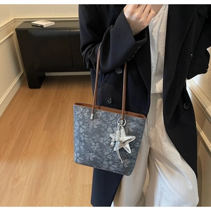 Close-up of floral tote bag with brown leather handles and star charm on dark blazer