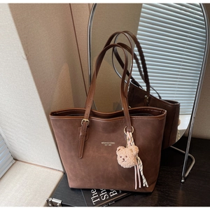 Detail of dark brown matte tote bag with gold logo lettering and plush bear charm