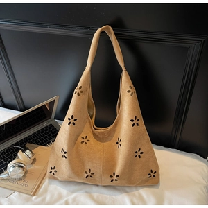 Brown laser-cut hollow tote bag in suede texture with floral patterns on a white bed