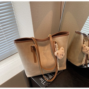 Detail of khaki suede tote bag featuring contrast brown straps and a cute plush bear charm