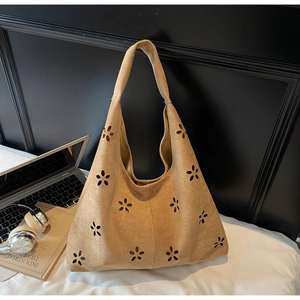 Detail of laser-cut floral patterns on khaki suede tote bag in a modern office setting