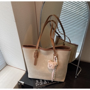 Detail of beige tote bag featuring brand lettering, bear charm and stylish striped scarf