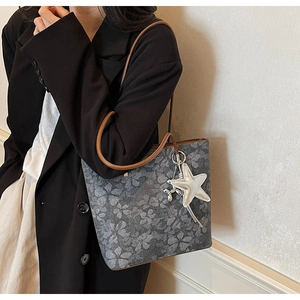 Close-up of grey floral tote bag with brown leather straps and star charm detail