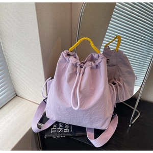 Dettaglio dello zaino viola con manico giallo e chiusura a coulisse su piano in legno