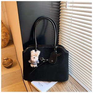 Detail of black suede tote bag with patent leather handles and white plush puppy charm