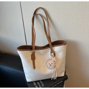 Detail of minimalist cream tote bag with brown straps and plush bear charm on art book