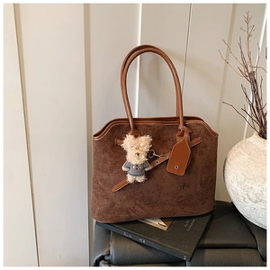 Detail view of a dark brown suede tote bag featuring a cute bear charm and curved edge design