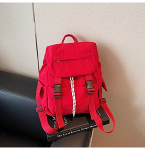 Detail of red nylon backpack with dual buckles and white drawstring on a black book
