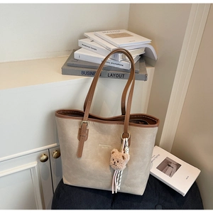 Detail of beige tote bag with brown straps, teddy charm, and checkered scarf decoration
