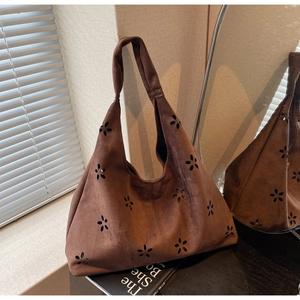Detail of brown suede tote bag with laser-cut floral patterns in a natural light setting