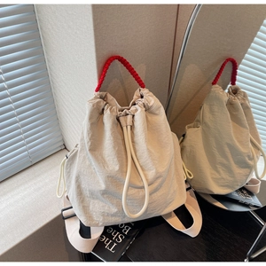 Dettaglio dello zaino in tela beige con manico intrecciato rosso e chiusura a cordoncino