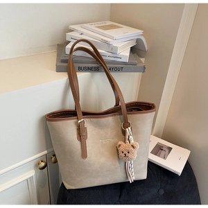 Detail of vintage beige tote bag with brown leather trim and cute plush bear keychain