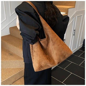 Close-up of a large brown suede tote bag with wide shoulder strap worn by a model