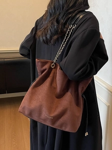 Sac seau en daim marron avec bandoulière chaîne dorée et cordon, porté par le mannequin