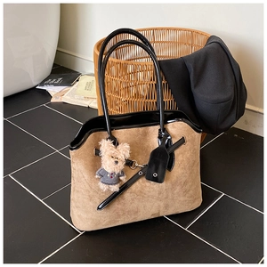 Detail of suede tote bag with leather trim and cute bear charm on marble floor