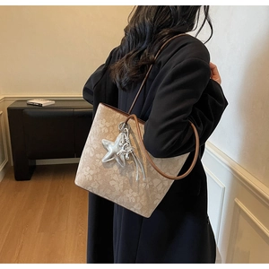 Detail of beige floral tote bag with brown straps and star pendant on a model's shoulder