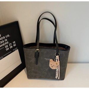 Detail of dark gray tote bag with gold lettering and cute bear plush charm accessory