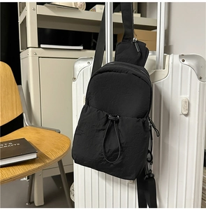 Detail of black nylon chest bag with drawstring texture hanging on a white suitcase