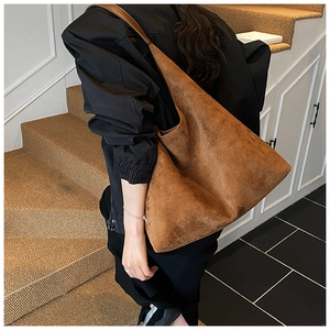 Close-up of a large brown matte tote bag with wide strap worn on a woman's shoulder